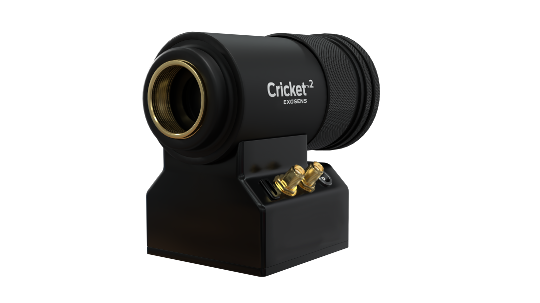 Black, cylindrical Cricket™2 imaging device mounted on a compact base, featuring a large front optical lens, textured grip rings, and front-panel controls and connectors; branded “Exosens” on the base, shown against a white background.